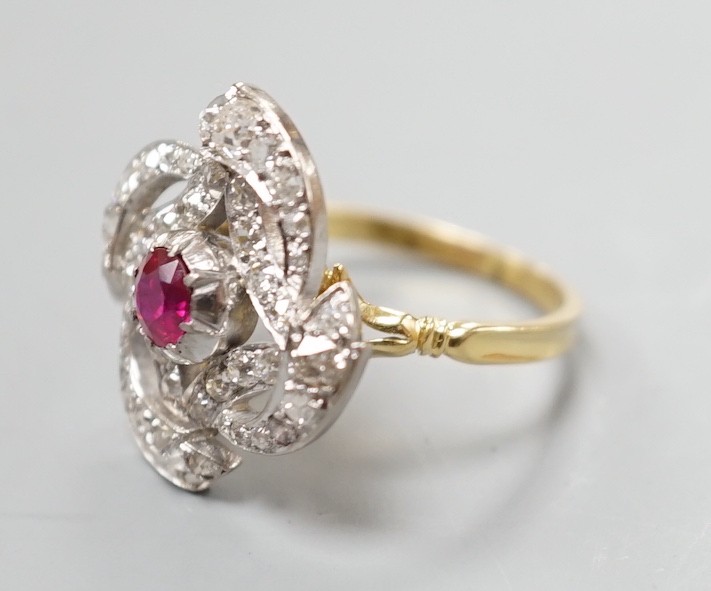 A yellow metal, ruby and diamond cluster set dress ring, in a pierced scroll setting, size O, gross weight 6 grams.